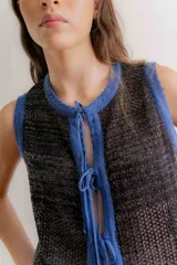 Chaleco tejido sin mangas, color negro, con textura brillante (lurex) y ribetes en azul. Presenta un escote redondo y se ata al frente con cordones.