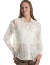 Camisa de tencel color blanco roto, semitransparente, con bordados florales en blanco. Tiene cuello con solapa, cierre frontal con botones decorados y un bolsillo en el pecho.