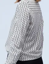 Camisa de manga larga, color blanco y negro, con cuello con solapa y abertura central con botones ocultos. Presenta un estampado geométrico repetitivo.