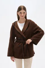 Chaqueta blanca de corte holgado con capucha, cierre frontal cruzado con botones y cinturón de tela ajustable. Presenta detalles de costuras decorativas en color negro en los bordes, solapas, bolsillos y cinturón.