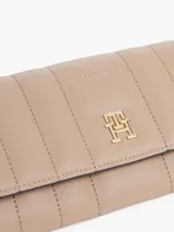 Billetera Tommy Hilfiger de poliuretano color beige, con diseño acolchado, cierre de solapa y logo metálico dorado TH en el frente.