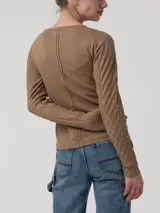 Remera de manga larga color beige, con cuello redondo y cierre frontal parcial con botones. Presenta un diseño de tejido trenzado con textura de rombos en las mangas y cuerpo liso.