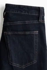 Jean de tiro alto con corte acampanado desde la rodilla, confeccionado en denim oscuro con cinco bolsillos y cierre frontal con botón.