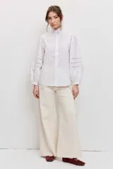 Camisa blanca de manga larga abullonada con detalles de encaje calado en las mangas y cuello alto con volado.