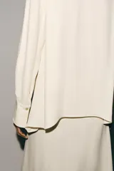 Blusa de viscosa color marfil, con cuello mao, manga larga con puños anchos, cierre frontal con botones y detalle de lazada colgante en el frente.