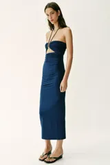 Vestido midi de color azul marino con escote halter y tirantes finos ajustables. Presenta un diseño con drapeados frontales y laterales, detalle cut out en el pecho con fornituras metálicas doradas y falda de corte evasé.