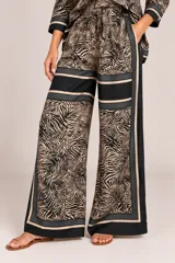 Palazzo de pierna ancha confeccionado en satén con estampado de animal print tipo cebra en tonos camel y negro, con detalles de bandas laterales y franja horizontal. Cuenta con cintura elástica fruncida y cordón ajustable.