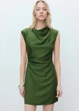 Vestido corto de color verde, confeccionado en tejido de modal con textura. Presenta un diseño entallado con cuello drapeado, sin mangas y detalle de drapeado lateral en la cintura. Incluye cierre de cremallera en la parte posterior.