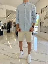 Camisa de lino a rayas celestes y blancas, con cuello mao y botones frontales en tono marrón.
