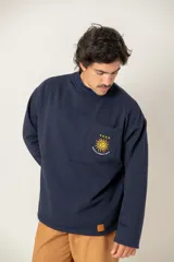 Buzo de cuello redondo color azul marino, con manga larga y corte holgado. Presenta un bolsillo frontal en el pecho con un bordado del sol de la bandera uruguaya, cuatro estrellas y la frase 'Heroicos sabremos cumplir'.