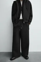 Pantalón de corte wide fit confeccionado en tejido técnico con efecto neopreno. Presenta cintura elástica ajustable con cordón, perneras anchas con costura frontal, bolsillos laterales y bolsillos traseros de plastrón.