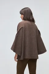 Capa de lana fina sin teñir, con diseño de corte amplio y mangas tipo kimono. Presenta cierre frontal mediante tres alamares de cuero en tono marrón.