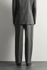 Pantalón de traje gris de corte relaxed fit, confeccionado en pura lana, con bolsillos laterales, bolsillos traseros de doble vivo y raya marcada en las piernas.
