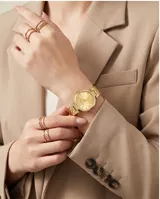 Reloj analógico de mujer con caja redonda y malla de eslabones metálicos, acabado en tono dorado. Presenta una esfera minimalista con marcadores de hora y detalles brillantes.