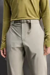 Pantalón de hombre color marrón oscuro, corte regular fit, confeccionado en tejido técnico compacto elástico. Presenta cintura ajustable con cinturón negro a contraste, bolsillos frontales, bolsillo trasero con cierre y bolsillo cargo con cierre en la pernera.