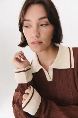 Sweater de punto color marrón con cuello polo en contraste color crema. Presenta diseño de rayas verticales texturizadas, mangas largas con puños en color crema y corte holgado.