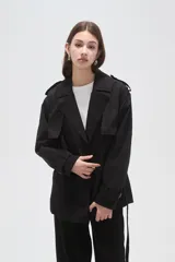 Trinchera de corte corto y diseño clásico, confeccionada en poliéster color negro. Presenta solapas amplias, cierre frontal cruzado con lazo ajustable en la cintura, charreteras en los hombros y puños con trabillas.