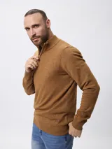 Sweater de tejido de punto color tostado, con cuello alto y cierre frontal parcial. Presenta mangas largas con puños acanalados y un pequeño detalle bordado en el ruedo.