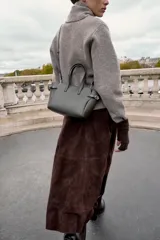 Bolso mini shopper de color gris oscuro, con diseño estructurado, doble asa de mano y correas laterales decorativas con hebillas metálicas. Incluye cierre magnético y compartimento interior con cremallera.