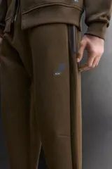 Pantalón jogger de entrenamiento, corte regular fit, color verde oliva oscuro. Confeccionado en tejido técnico compacto de algodón con elasticidad y efecto neopreno. Presenta cintura elástica ajustable con cordón blanco, bolsillos frontales y un bolsillo lateral con cierre de cremallera. El bajo termina en puño.