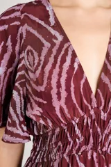 Vestido largo con estampado animal print abstracto en tonos bordó y rosado. Presenta escote en V, mangas cortas con volados y cintura elástica fruncida.