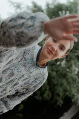 Buzo de tejido de punto calado con diseño de red, cuello redondo y mangas largas abullonadas. Presenta una textura jaspeada en tonos gris y blanco.