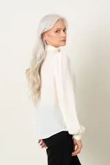 Blusa color marfil de manga larga con frunce en hombros y puños, escote en V con lazo y cierre de puños con dos botones.