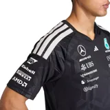 Camiseta técnica de manga corta Adidas del equipo Mercedes-AMG Petronas F1, color negro con estampado geométrico sutil y múltiples logotipos de patrocinadores en el frente y mangas. Presenta cuello en V con detalle en color turquesa y las icónicas tres tiras de Adidas en los hombros.