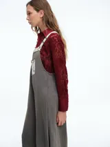 Mono largo de color negro con corte holgado y perneras anchas. Presenta detalles de encaje blanco y tela estampada floral en los tirantes, el bolsillo frontal, la parte inferior de las piernas y el ruedo.