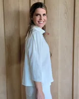 Camisa de manga tres cuartos color beige con cuello con volados y botones frontales. Presenta un detalle de color negro en la parte superior de las mangas.