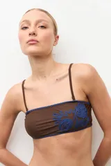 Top de bikini bandeau color azul con detalle de bordado floral en hilo crudo en el lateral.