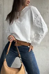 Blusa blanca de lino con mangas largas abullonadas, destacada por paneles laterales bordados con detalles de encaje. Presenta un corte holgado y cuello redondo.