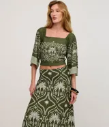 Pollera larga (midi/maxi) de tejido piqué, color verde oscuro con estampado en blanco/beige de motivos tropicales y palmeras. Presenta un diseño con fruncido en la parte inferior.