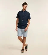 Bermuda de hombre en lino color gris claro, de corte recto, con textura discreta, bolsillos laterales y cierre frontal con botón y cremallera.