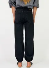 Pantalon de denim azul oscuro con diseño abombado y puños fruncidos con elástico en los tobillos. Cuenta con bolsillos laterales y cierre frontal con botón y cremallera.