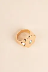 Anillo dorado con forma de flor y detalle de cristal iridiscente en el centro.