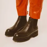 Botas negras de cuero estilo chelsea, con suela track gruesa y elásticos laterales. Presentan una tira vertical de cuero marrón en la parte posterior.