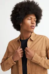 Camisa marrón de manga larga con cuello clásico, cierre frontal con botones, dos bolsillos con solapa abotonada en el pecho y puños abotonados.