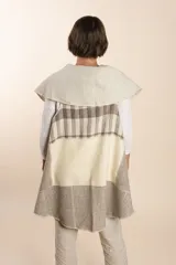 Chaleco sin mangas de tejido de lana fina sin teñir, con diseño circular y bloques de color beige y marrón. Presenta un cuello amplio y solapa que permite usarlo como chaleco largo o capa corta.