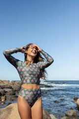 Top de bikini de manga larga con cuello redondo y espalda descubierta, confeccionado en lycra con protección solar. Presenta un estampado integral de caracoles en tonos rosados sobre una base verde con acabado brillante.