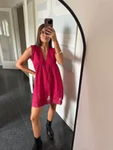 Vestido corto color fucsia, con escote en V profundo y mangas cortas tipo volado. Presenta un diseño con textura de bordado inglés o perforado y un corte imperio con frunce que da volumen a la falda.