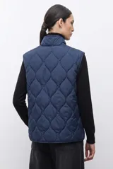 Chaleco capitoneado reversible con cuello alto, cierre frontal con botones a presión y bolsillos delanteros. Presenta un diseño bicolor en tonos verde oliva y beige con detalles en negro.