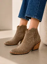 Bota corta estilo western confeccionada en gamuza color marrón oscuro, con taco de madera de diseño geométrico y puntera reforzada con detalle metálico.