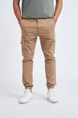 Pantalón cargo color beige, de corte slim fit, con bolsillos laterales tipo cargo, cierre frontal con botón y puños elásticos en los tobillos.