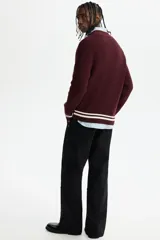 Buzo de punto acanalado en color bordó, con cuello en V y detalles de rayas blancas en contraste en los puños y el ruedo. Presenta un corte boxy que ofrece una silueta amplia y estructurada.