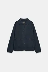 Chaqueta oversize de mezclilla color azul marino, de cuello solapa y manga larga, con bolsillos de parche en el delantero y cierre frontal con botones metálicos.