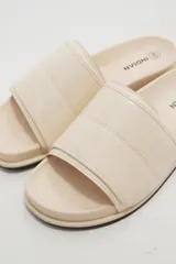 Sandalias planas color marfil, con tira ancha acolchada en el empeine y suela baja con borde oscuro.