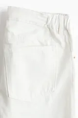 Jean tobillero blanco de corte recto y tiro bajo con detalles de bordado broderie en las piernas. Confeccionado en denim de algodón rígido, cuenta con cinco bolsillos, presillas para cinturón y cierre frontal con botón metálico.