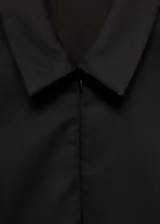 Vestido corto entallado de color negro, con cuello camisero y cierre frontal de cremallera invisible. Presenta mangas cortas y costuras decorativas verticales que realzan la silueta.