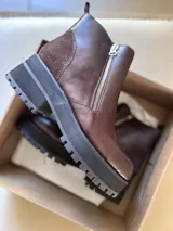 Botas cortas negras con plataforma dentada, confeccionadas en una combinación de cuero con textura de reptil y paneles de gamuza. Presentan un cierre frontal metálico y puntera cuadrada.